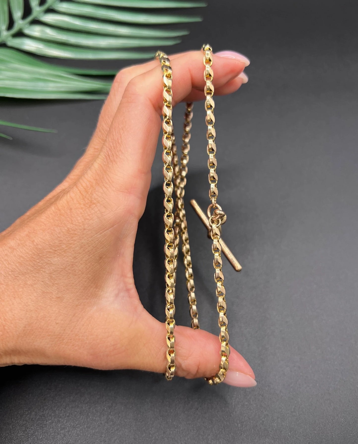 A rose gold tulip link chain necklace with a dog clip clasp and T-bar, held in a hand