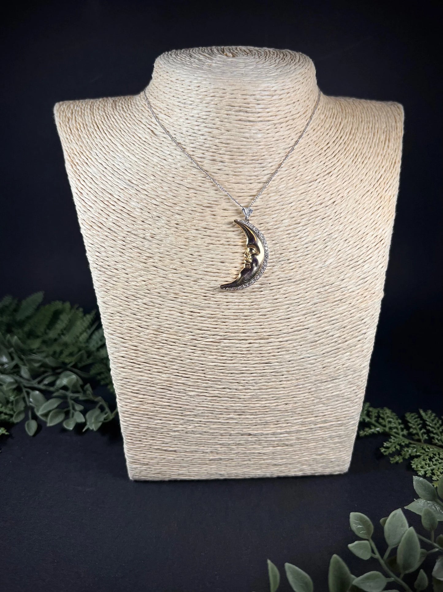 A gold crescent moon pendant with diamonds, on a chain, modelled on a jewellery bust