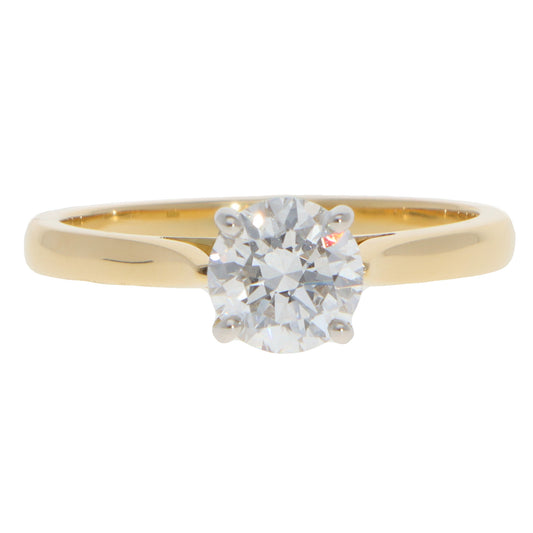 A yellow gold and platinum solitaire brilliant cut diamond ring, on a white background