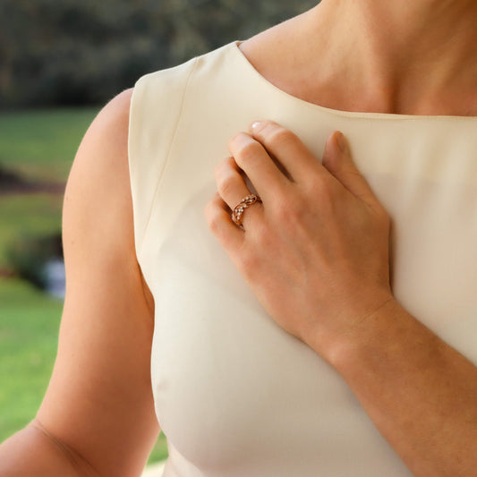 A rose gold diamond set foliate band modelled on a hand, held against a white dress