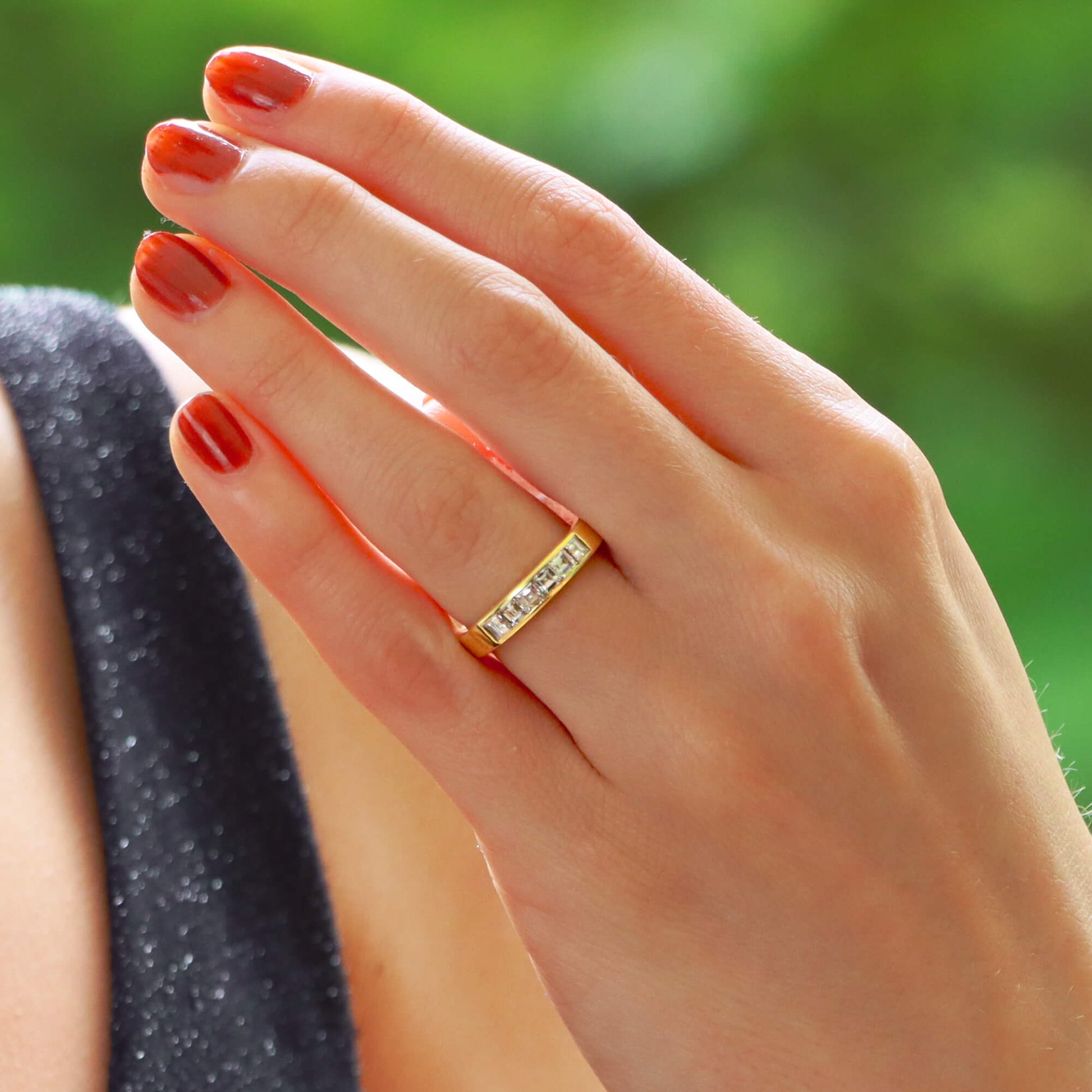 A yellow gold ring with six square diamonds, modelled on the ring finger of a woman wearing a black dress
