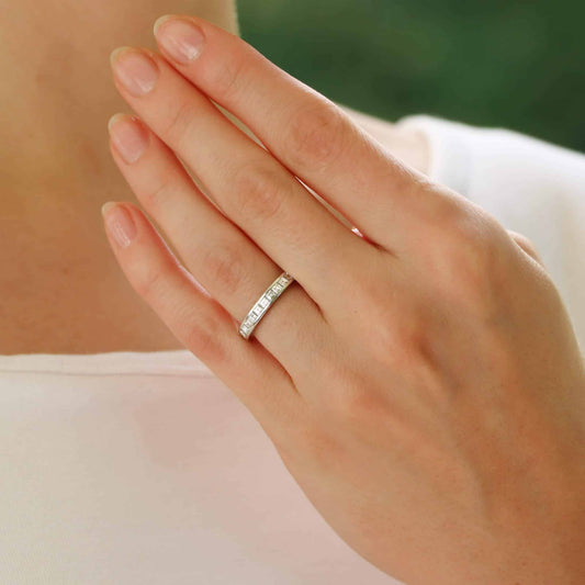 A platinum eternity ring with princess cut diamonds, modelled by a woman wearing a white dress