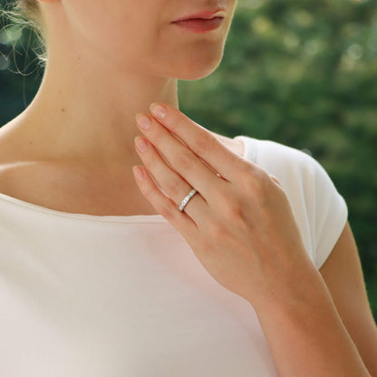 A platinum eternity ring with princess cut diamonds, modelled by a woman wearing a white dress