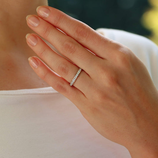 A white gold brilliant cut diamond eternity ring, modelled on the hand of a woman wearing a white dress