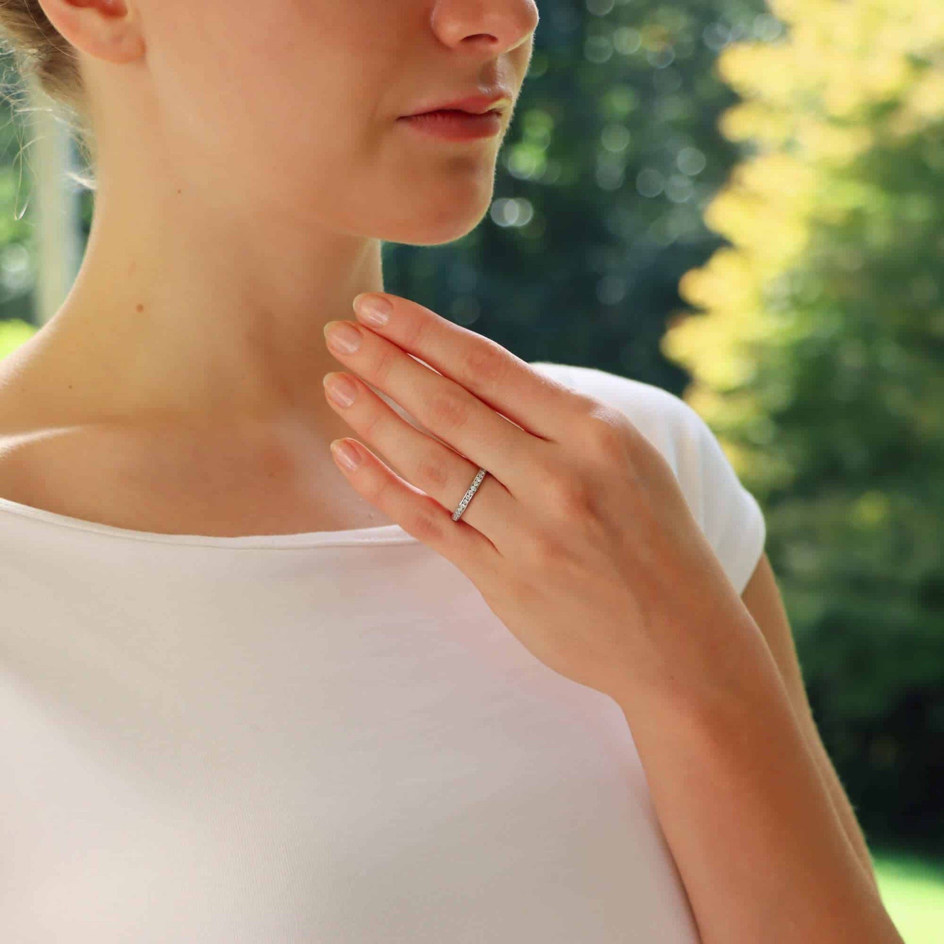 A white gold brilliant cut diamond eternity ring, modelled on the hand of a woman wearing a white dress