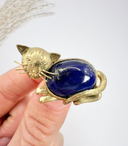 A yellow gold cat brooch with a lapis lazuli body, held in a hand