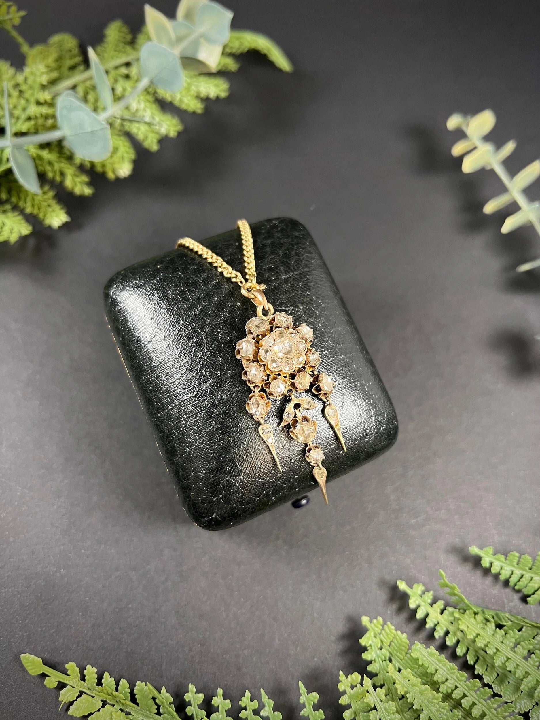 A yellow gold pendant with old cut diamonds, with a gold chain, on a black antique box