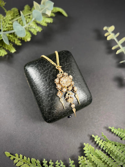 A yellow gold pendant with old cut diamonds, with a gold chain, on a black antique box