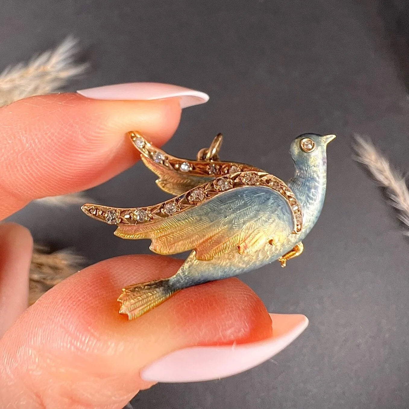 An enamel and diamond dove bird pendant, held in a hand