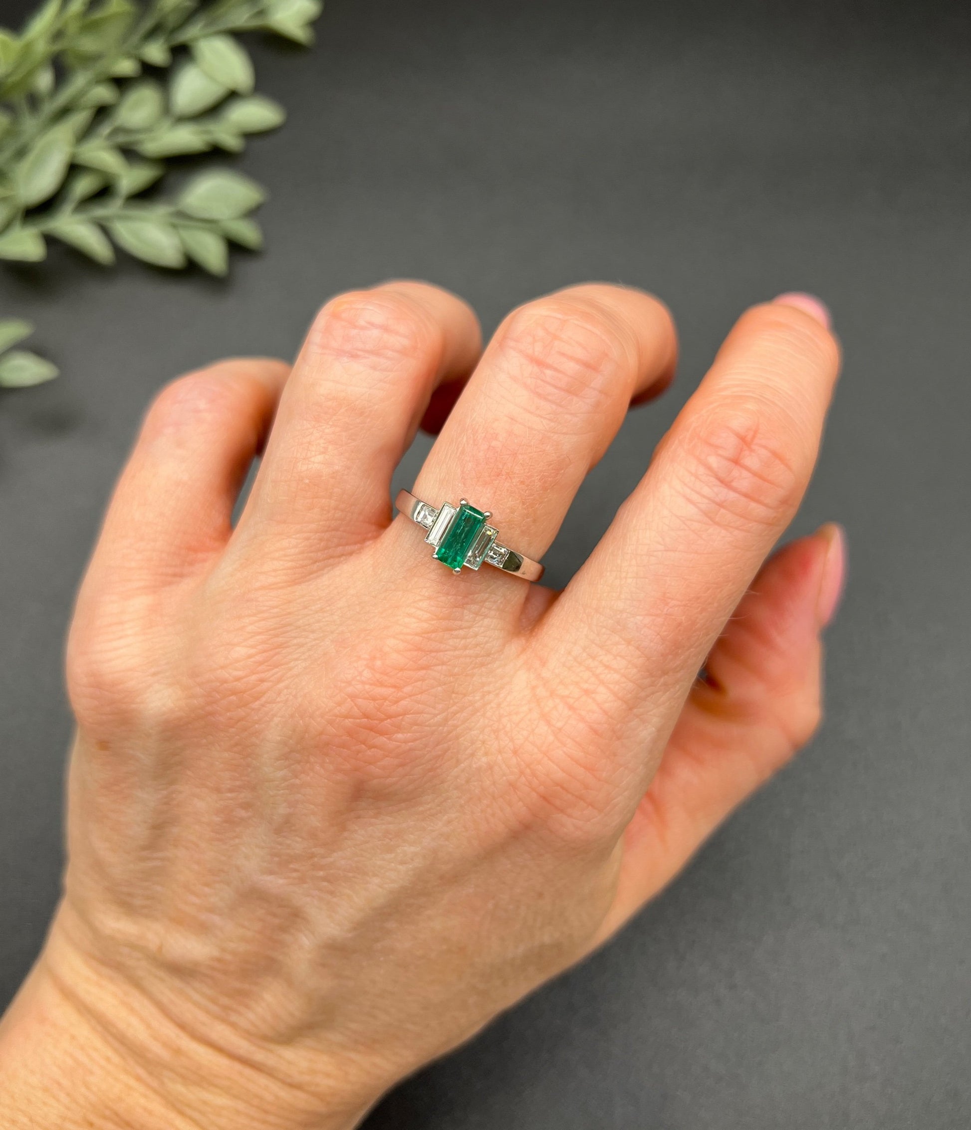 A five stone emerald cut emerald and baguette and square cut diamond ring in platinum, modelled on a hand