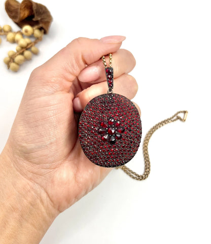 An antique oval locket encrusted with garnets, with a chain, held in a hand