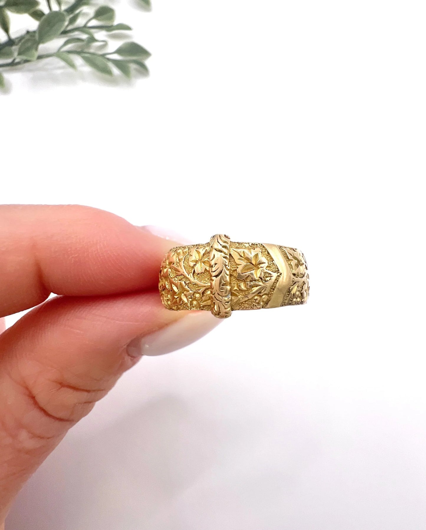 A yellow gold ornate engraved buckle band ring, held in a hand