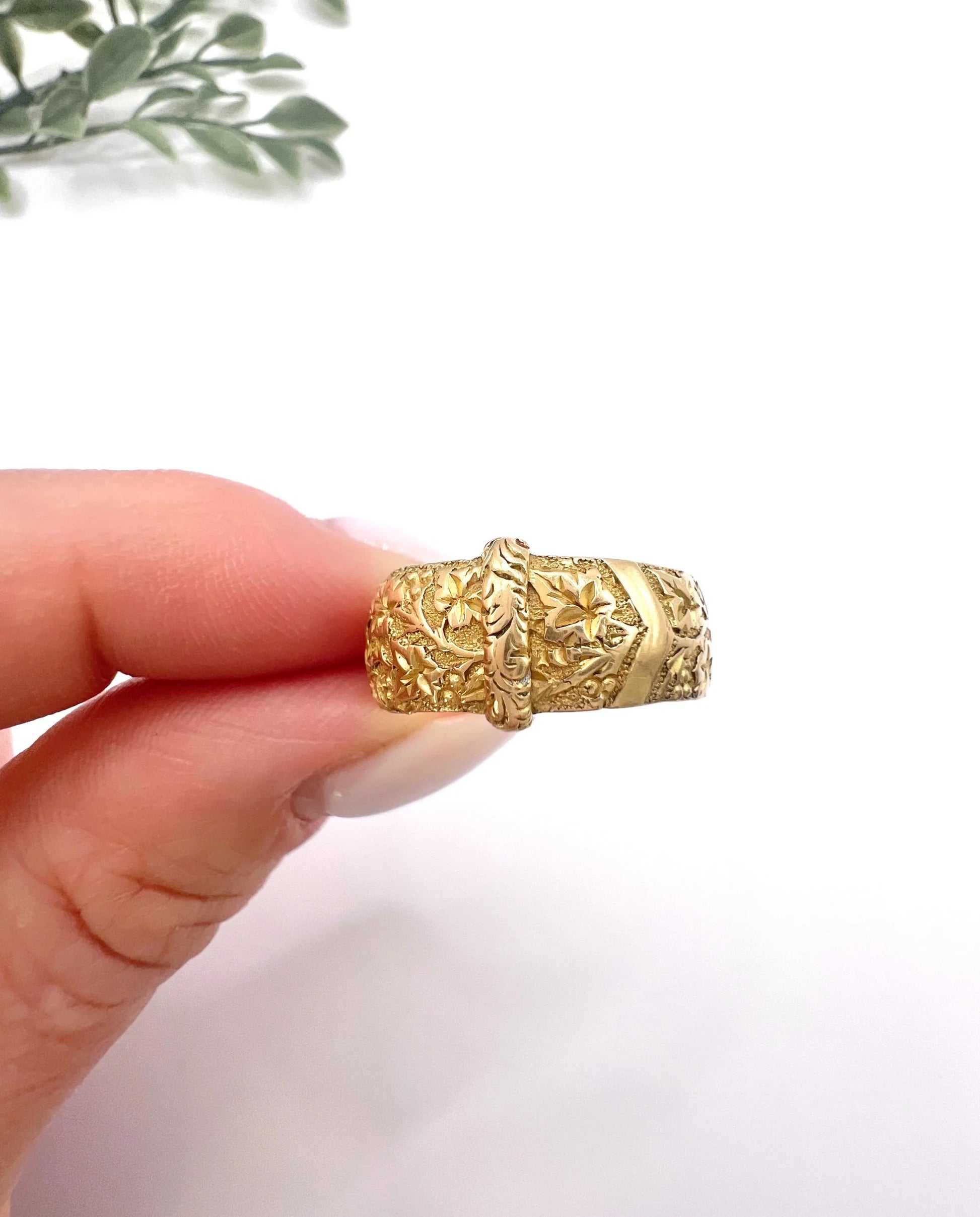 A yellow gold ornate engraved buckle band ring, held in a hand