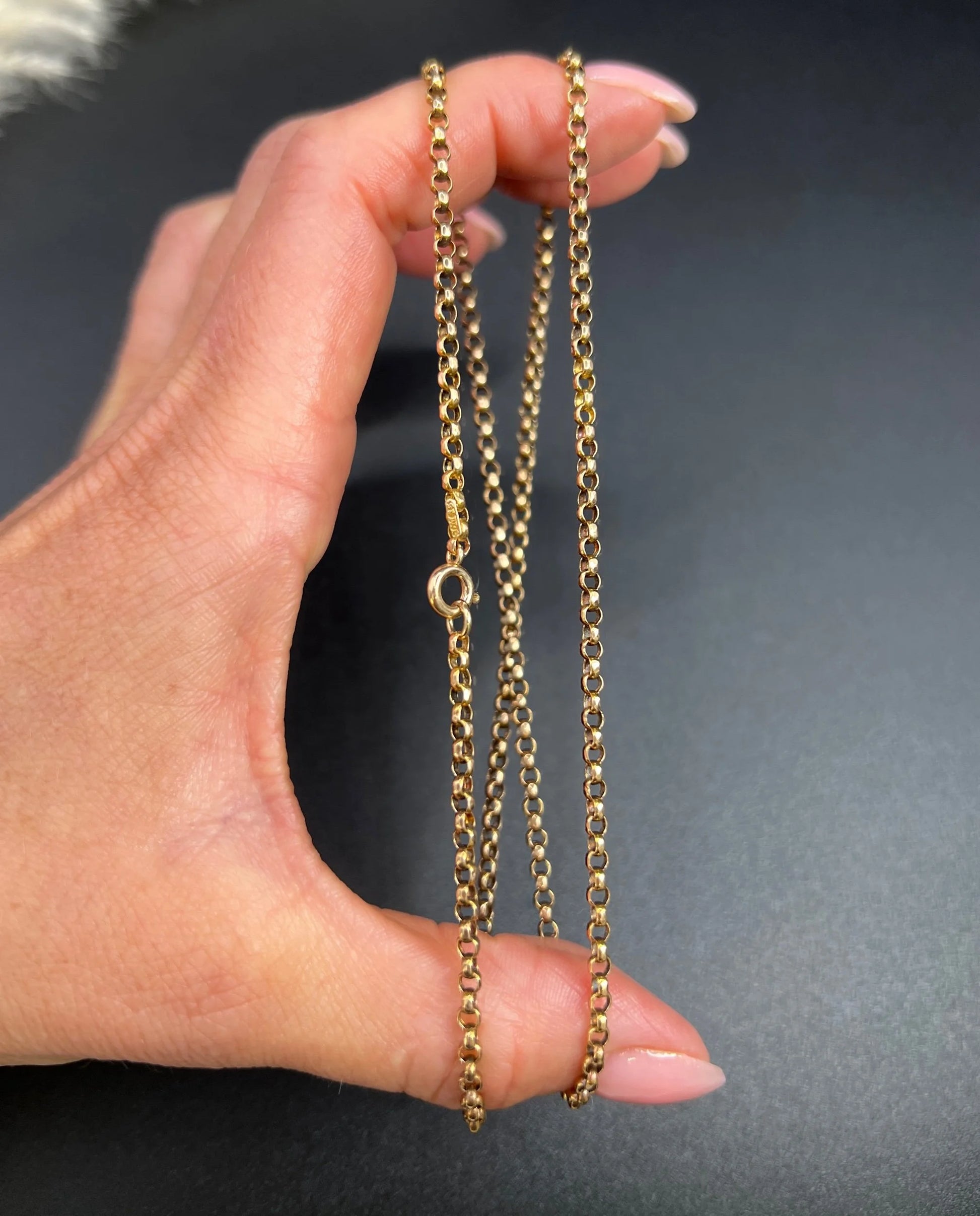 A gold belcher link necklace, held in a hand