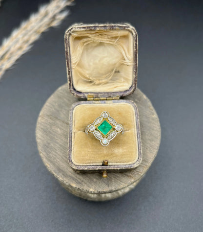 A gold and platinum ring with a centre emerald and diamond surround, in an antique ring box