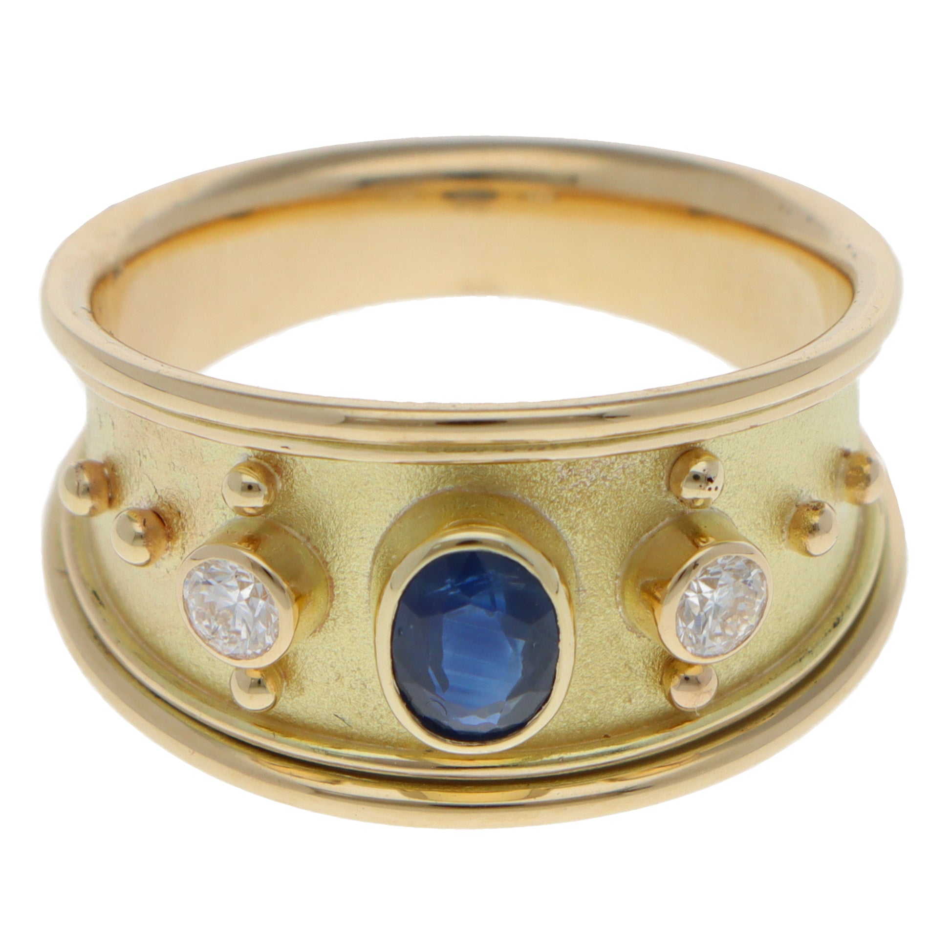 A yellow gold three stone band ring with an oval blue sapphire and two round diamonds, on a white background