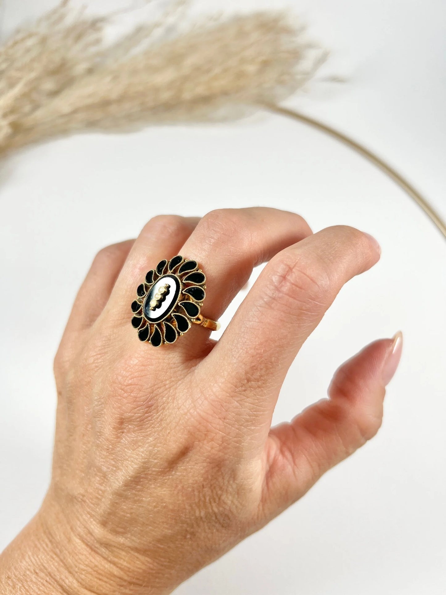 A black onyx and seed pearl fancy halo cluster ring in yellow gold, modelled on a hand