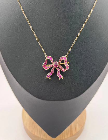 A ruby bow brooch necklace in gold and silver, on a black jewellery bust