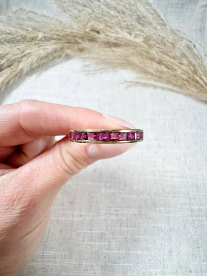 A yellow gold ruby channel set eternity band, held in a hand