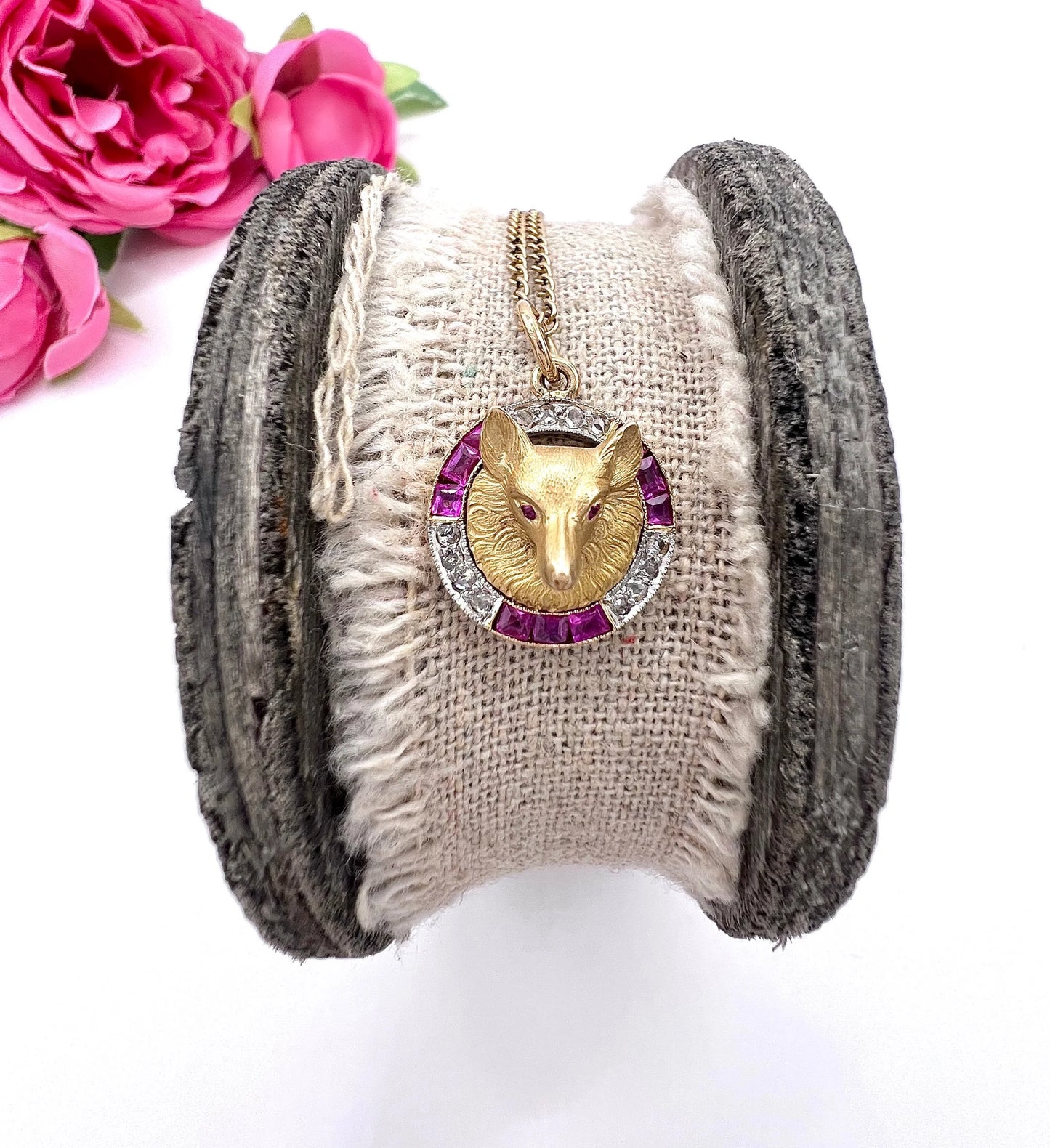 A fox head pendant in yellow gold with a ruby and diamond border, with a gold chain
