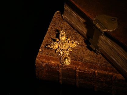 An ornate yellow gold cross pendant with table cut diamonds, next to antique books