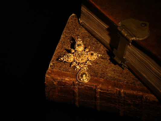 An ornate yellow gold cross pendant with table cut diamonds, next to antique books