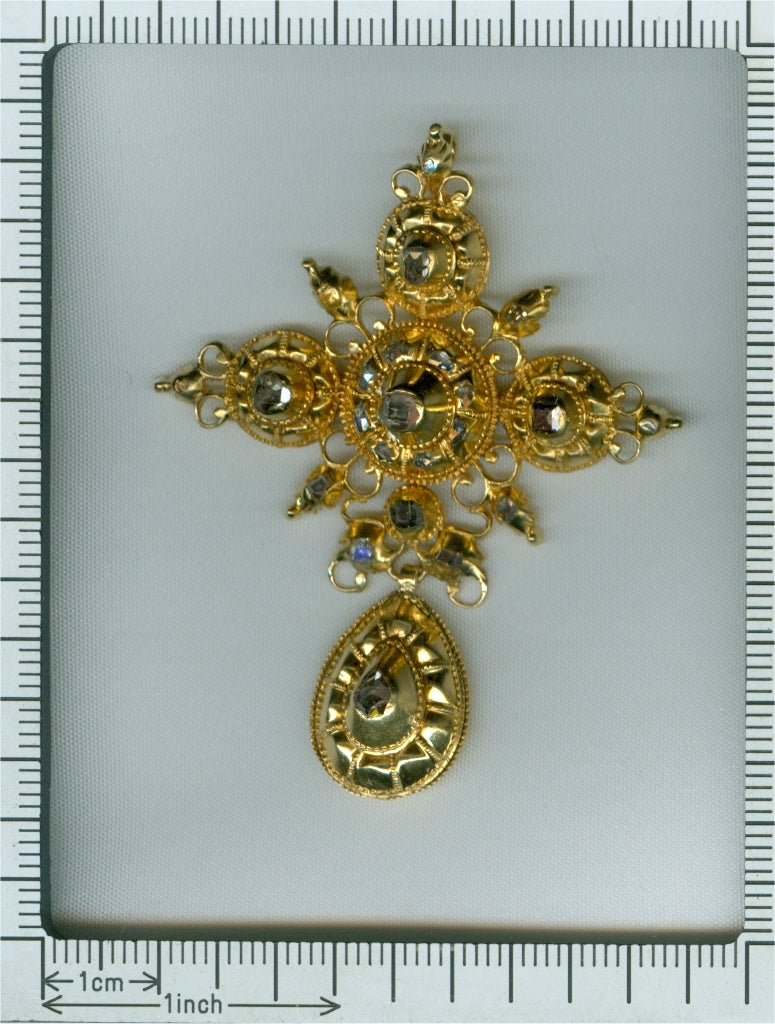 An ornate yellow gold cross pendant with table cut diamonds, next to a ruler