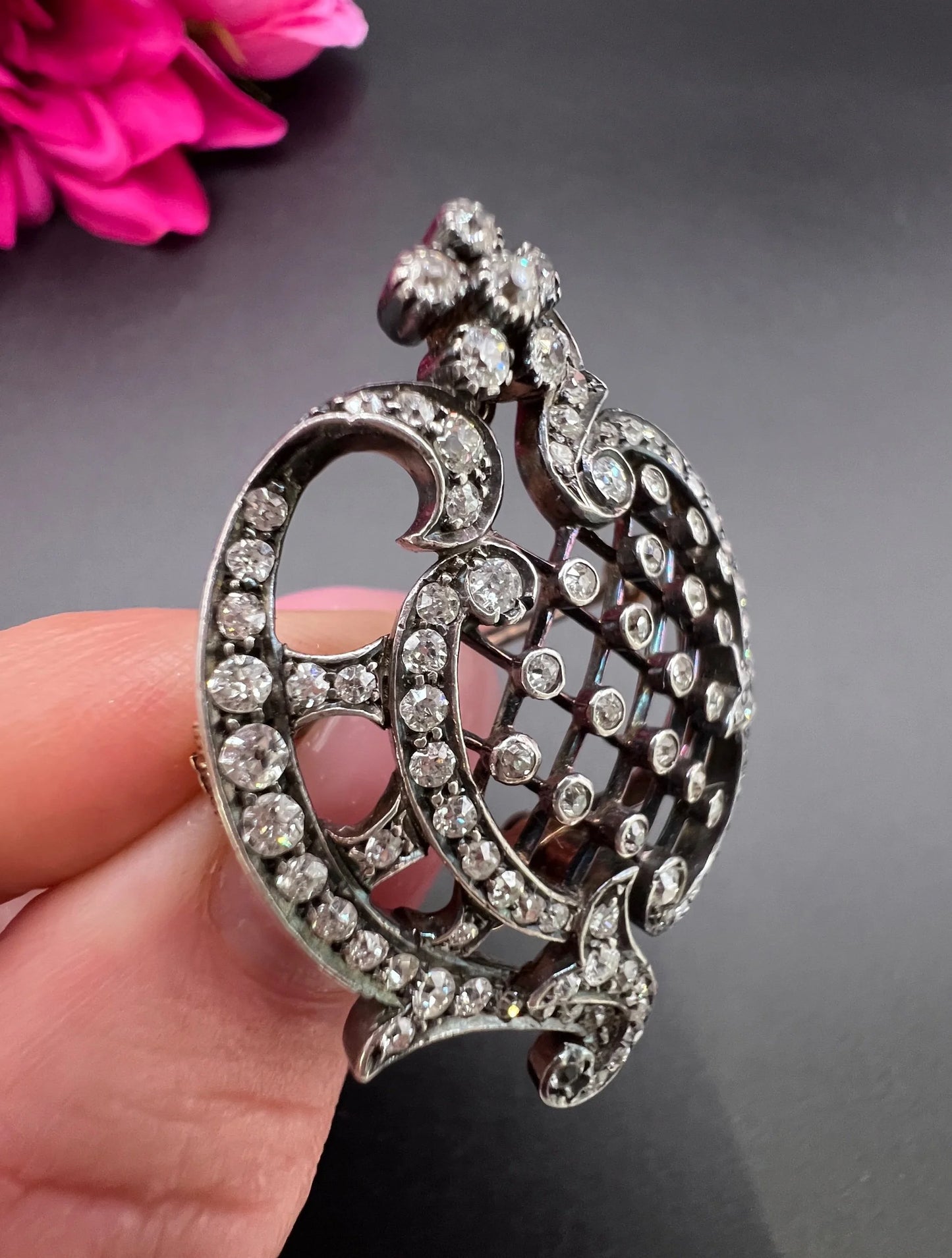 An openwork diamond set antique brooch in yellow gold and silver, held in a hand