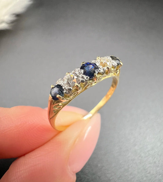 A yellow gold five stone sapphire and diamond carved half hoop ring, held in a hand
