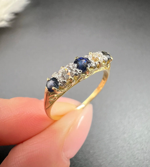 A yellow gold five stone sapphire and diamond carved half hoop ring, held in a hand