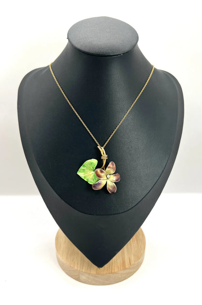 A gold and enamel diamond flower pendant with a gold chain, on a black jewellery bust