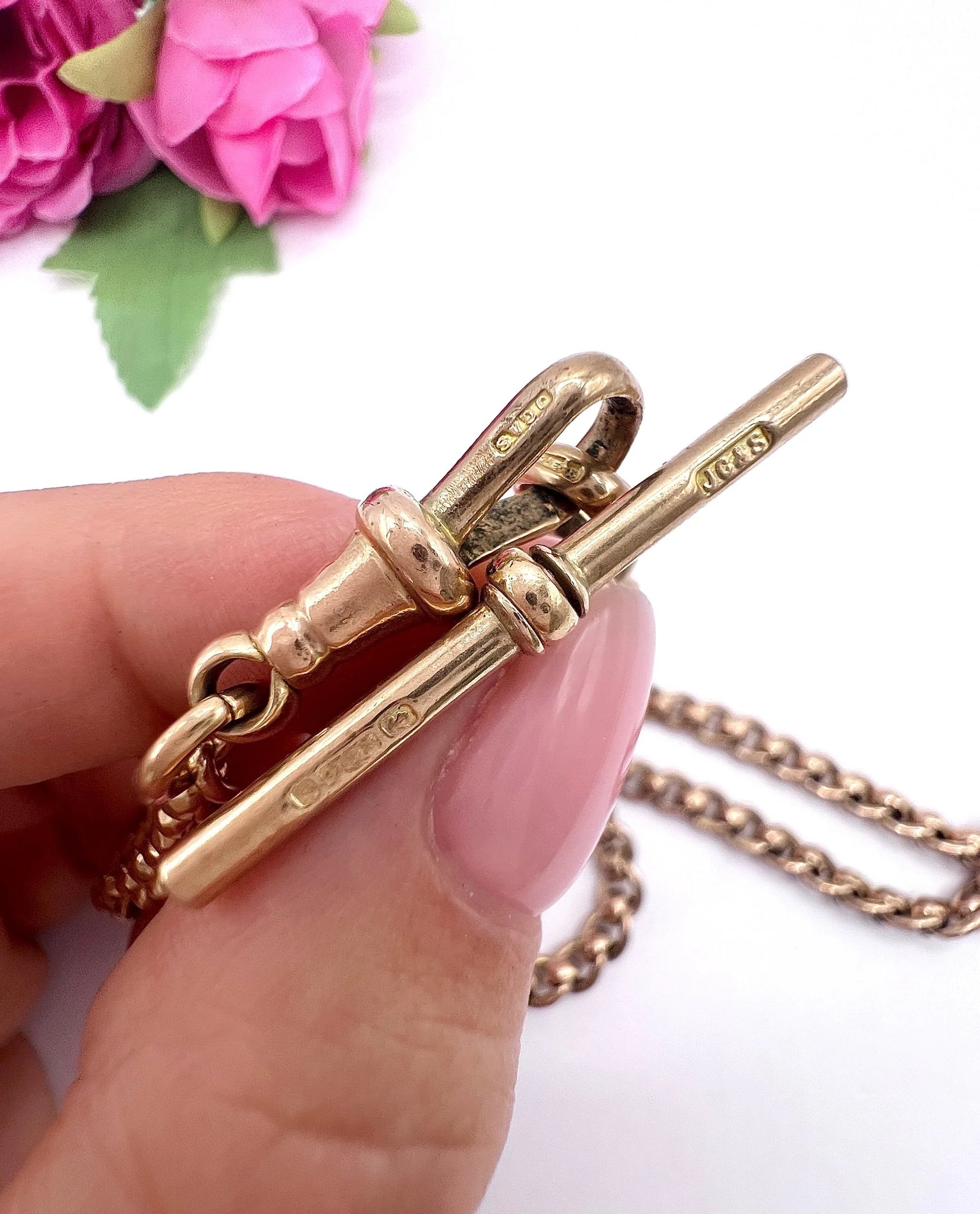A rose gold fancy link Albert chain necklace with a T-bar attachment, held in a hand