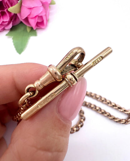 A rose gold fancy link Albert chain necklace with a T-bar attachment, held in a hand