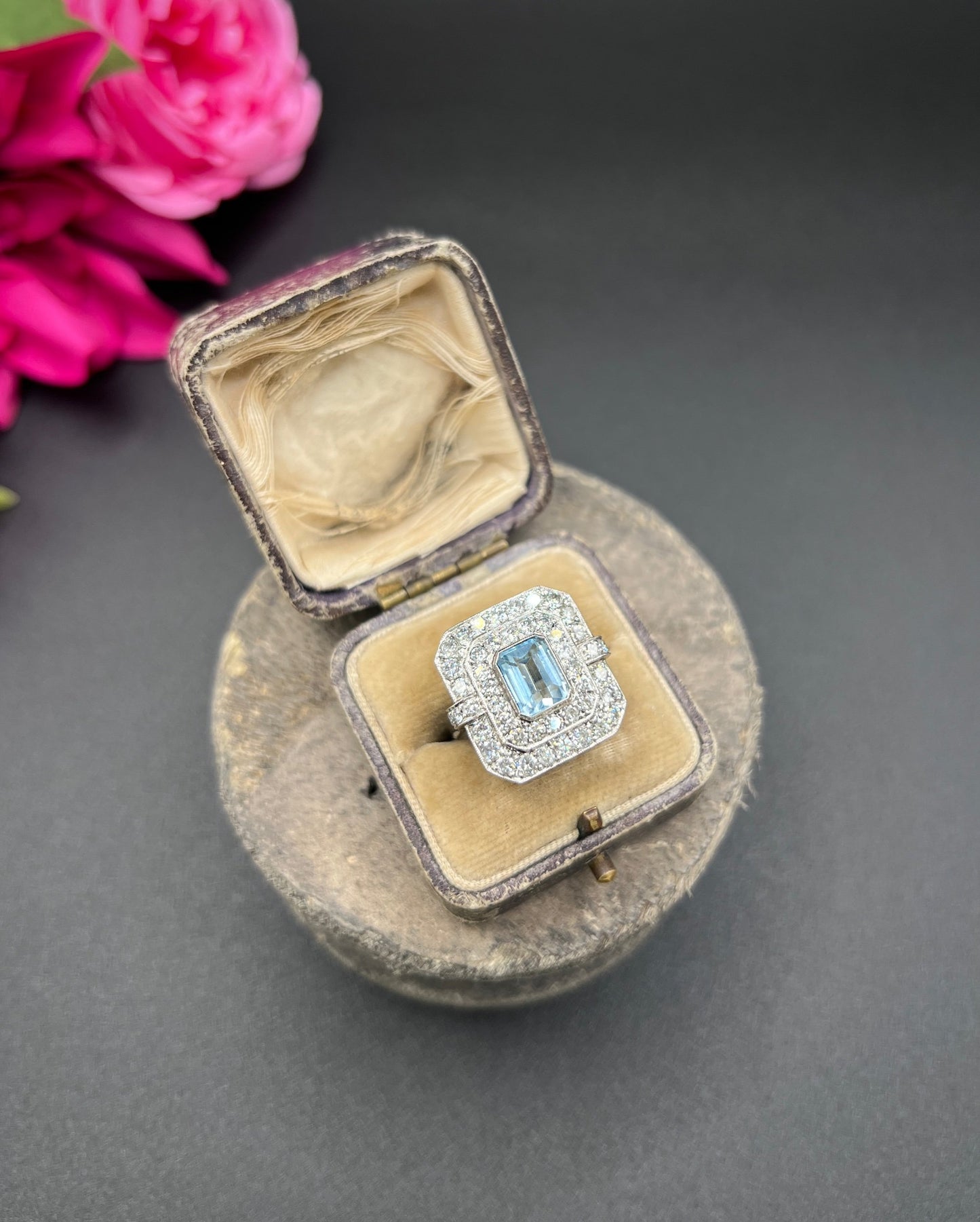 An octagonal shaped cluster ring with an aquamarine centre surrounded by two rows of diamonds, in platinum, in a ring box