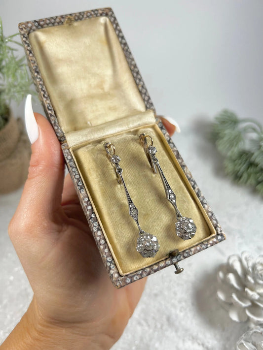 A pair of long drop earrings with diamonds, in an antique box held by a hand