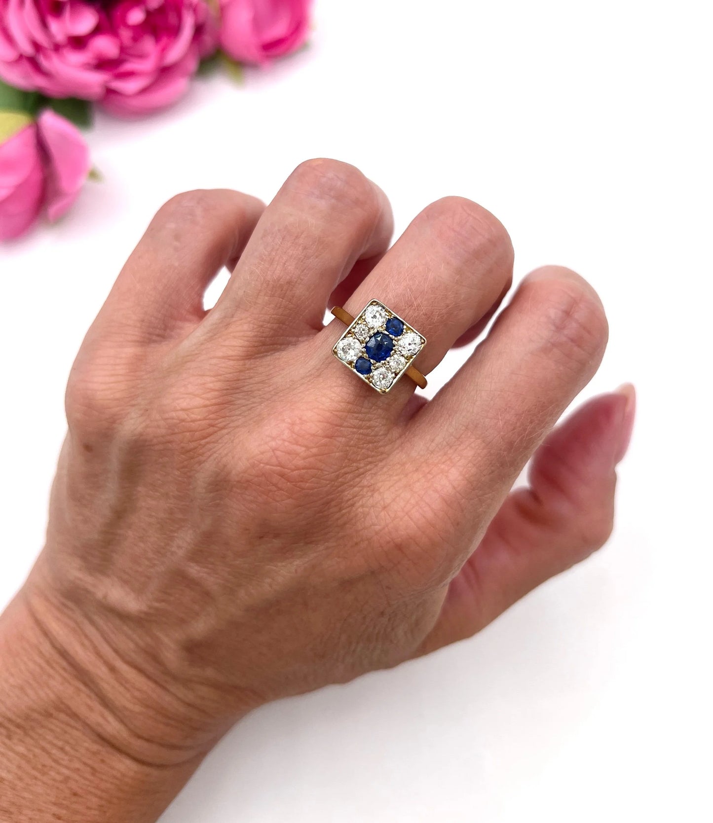 A square-shaped cluster ring with sapphires and diamonds in yellow gold and platinum, modelled on a hand