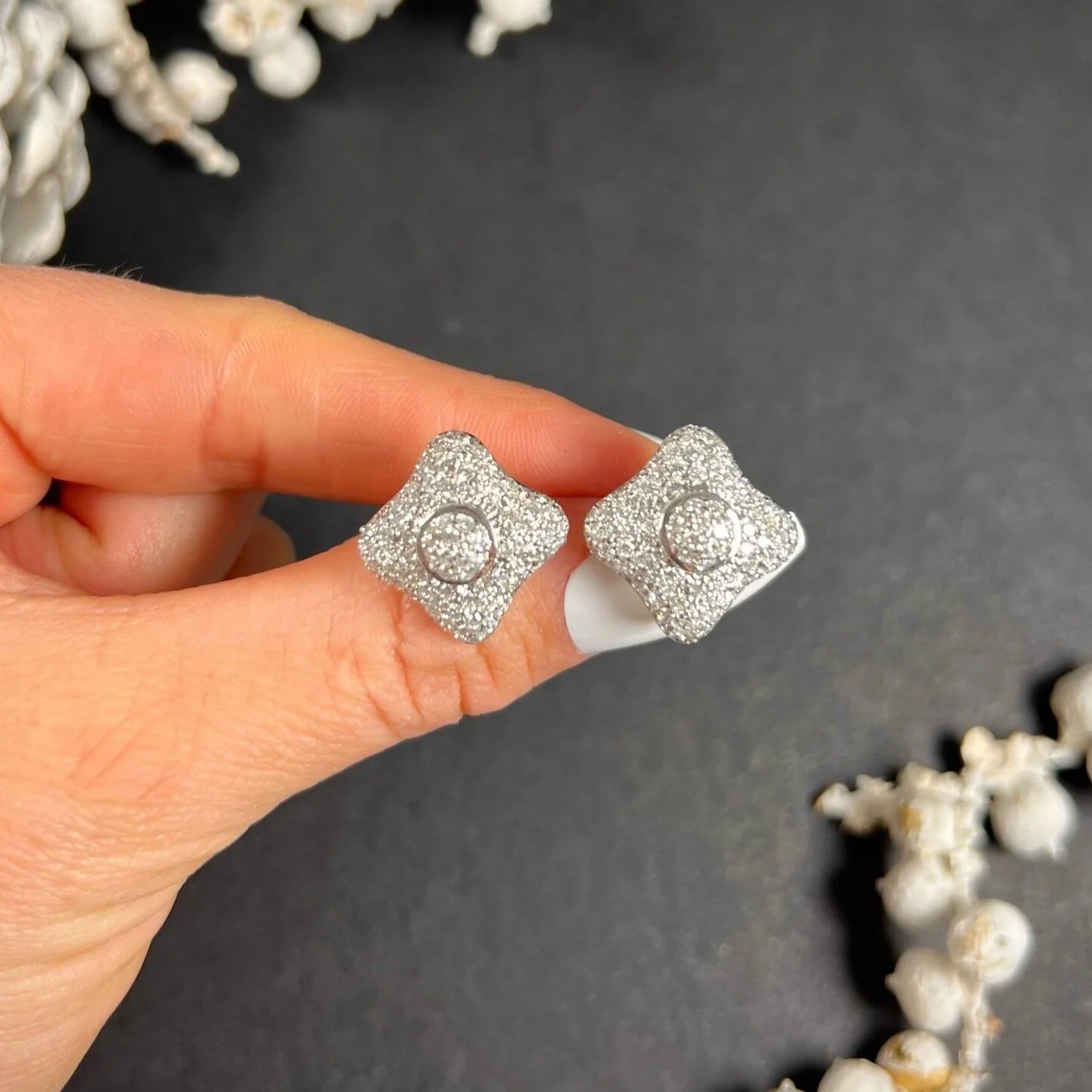 A pair of diamond cluster stud earrings in white gold, held in a hand