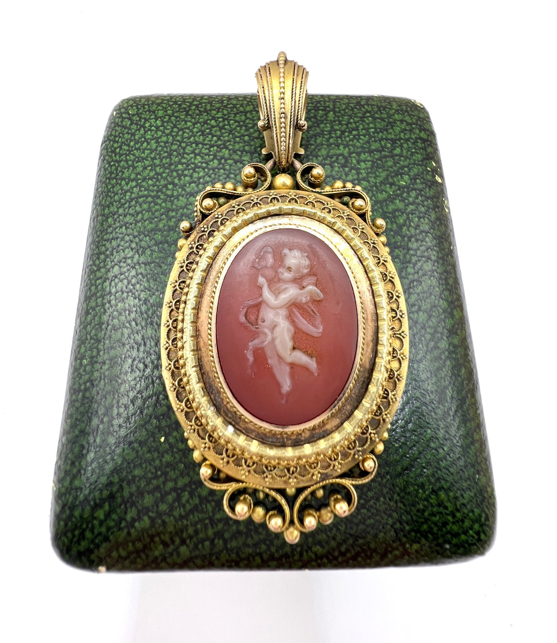 An ornate yellow gold oval cherub cameo locket pendant, on an antique box