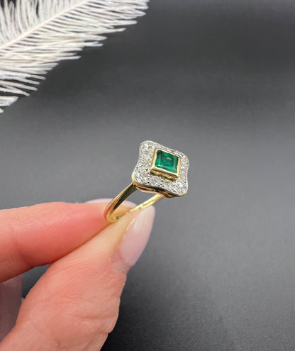 An emerald and diamond cluster ring in yellow gold and platinum, held in a hand