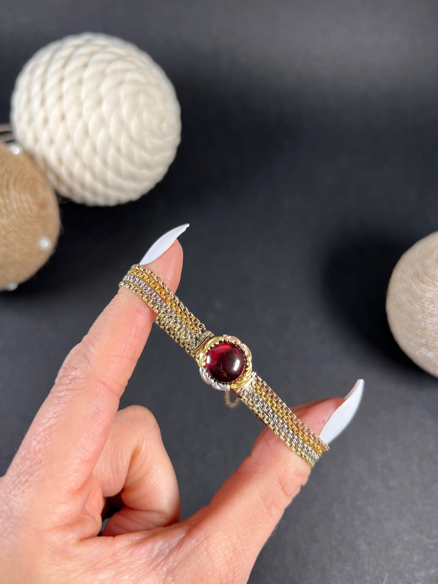 A cabochon garnet bracelet with three colour gold chains, held in a hand