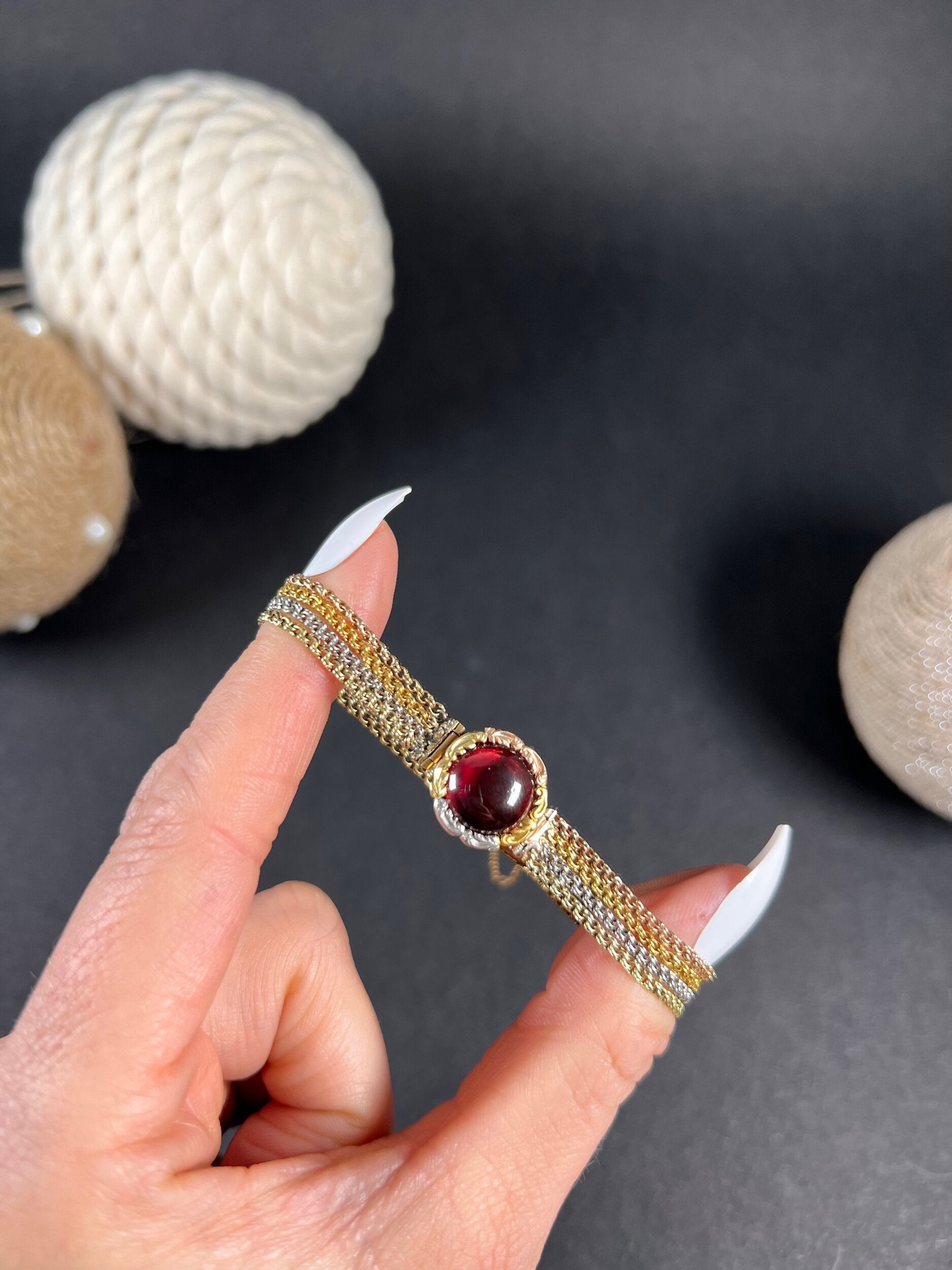 A cabochon garnet bracelet with three colour gold chains, held in a hand