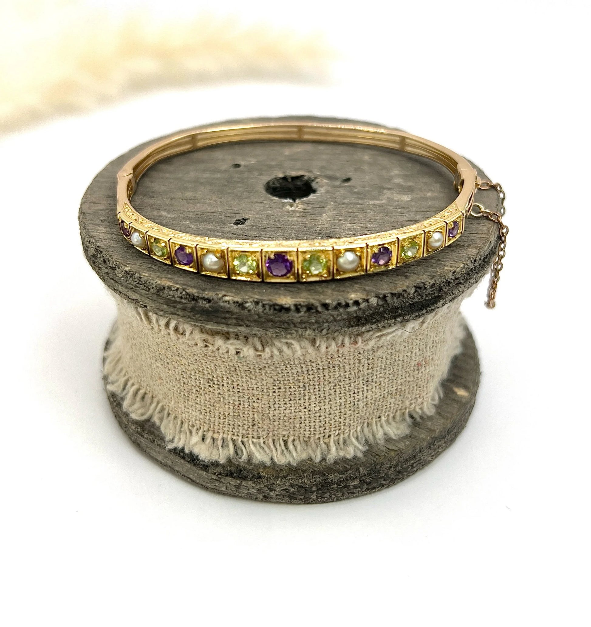 A yellow gold peridot, amethyst and pearl bangle bracelet, on a wooden spool