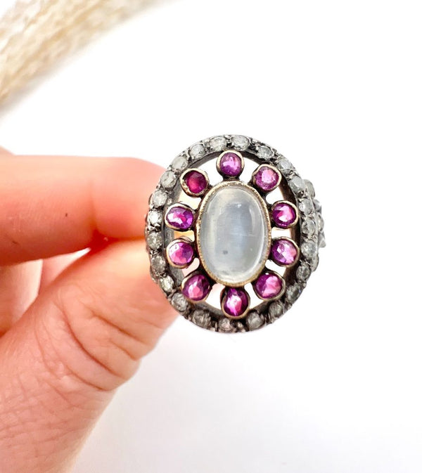 Early Victorian Antique Moonstone Ruby and Diamond Cluster Ring, oval cabochon moonstone surrounded by ruby petals within outer halo border of old-cut diamonds in silver to 18ct yellow gold. Mid 19th century Circa 1865