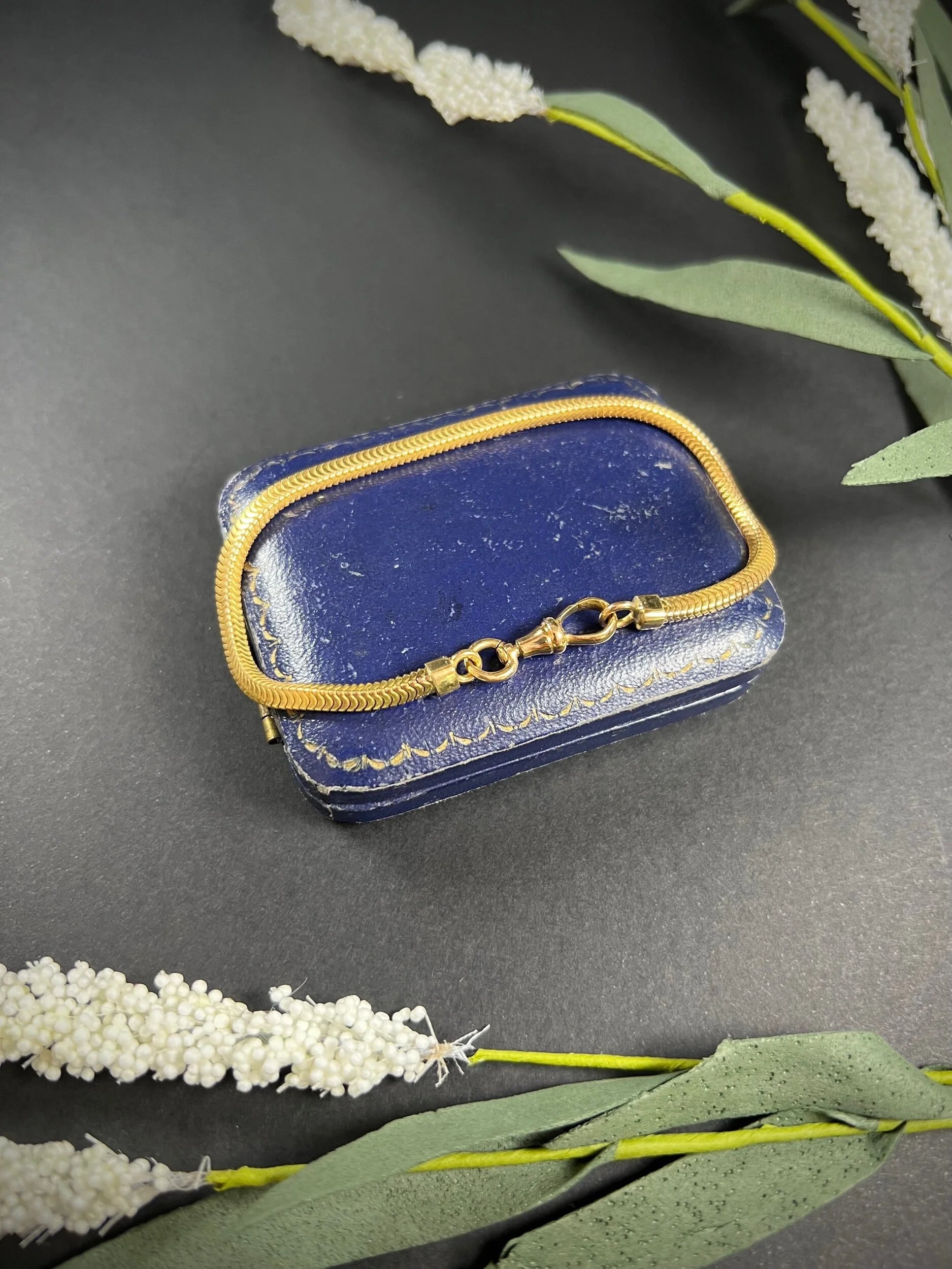 A yellow gold snake link bracelet, laid on a blue antique box