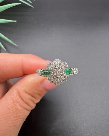 An emerald and diamond floral cluster ring in yellow gold and platinum, held in a hand