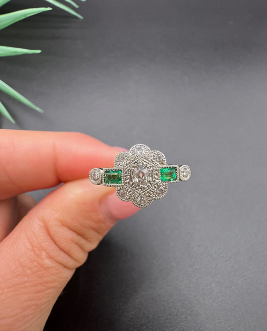 An emerald and diamond floral cluster ring in yellow gold and platinum, held in a hand