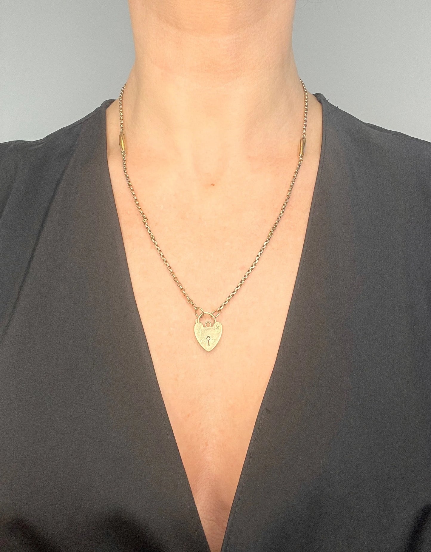 A yellow gold fancy link chain with a heart padlock, modelled by a woman
