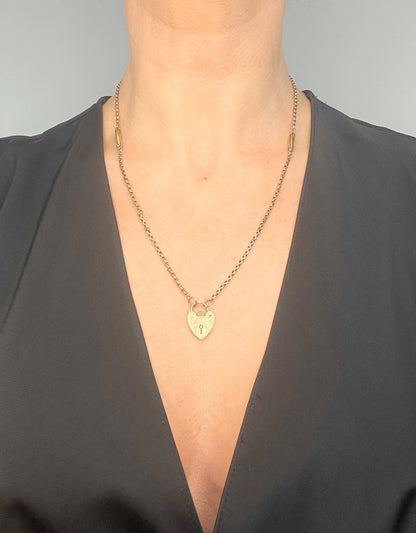 A yellow gold fancy link chain with a heart padlock, modelled by a woman