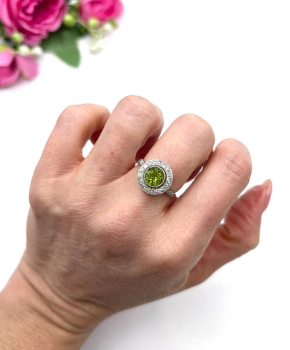 A white gold circular target cluster ring with a peridot centre surrounded by diamonds, modelled on a hand