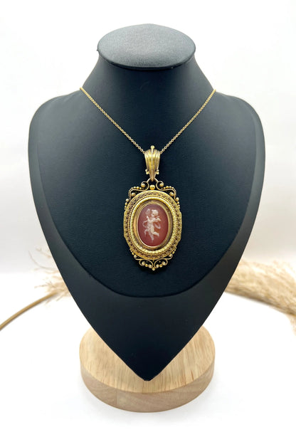 An ornate yellow gold oval cherub cameo locket pendant, with a chain, on a black jewellery bust
